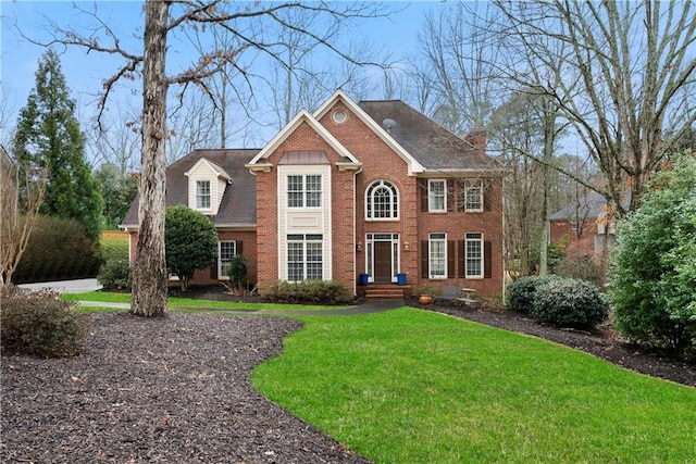 view of front of home with brick siding, a chimney, and a front lawn