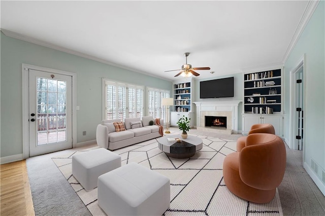 living area with a high end fireplace, baseboards, built in features, ornamental molding, and light wood-style flooring