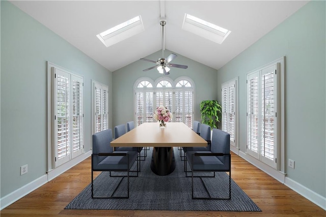 dining space featuring vaulted ceiling with skylight, ceiling fan, baseboards, and wood finished floors