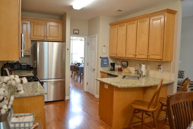 kitchen with sink, light stone counters, stainless steel appliances, light hardwood / wood-style floors, and backsplash