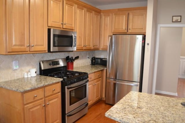 kitchen with light stone counters, stainless steel appliances, light hardwood / wood-style floors, and backsplash