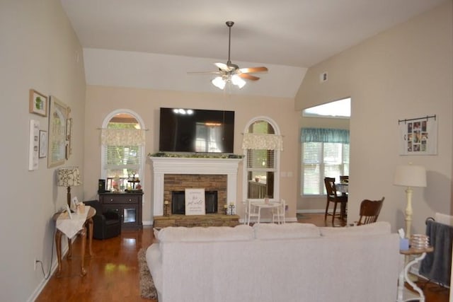 living room with vaulted ceiling, a stone fireplace, a healthy amount of sunlight, and dark wood-type flooring