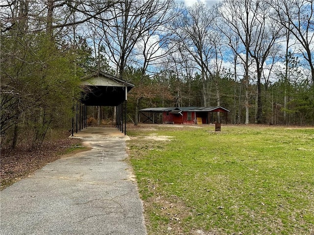 view of yard with aphalt driveway, a wooded view, a detached carport, and an outdoor structure