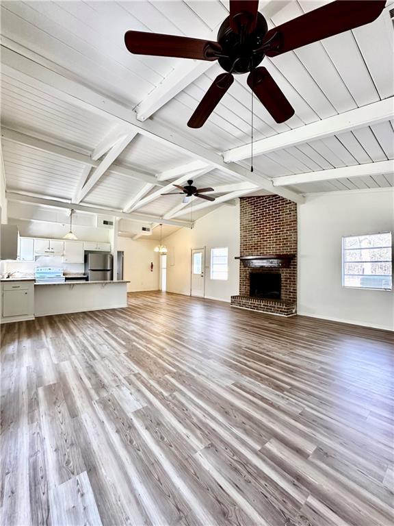 unfurnished living room with a brick fireplace, wood finished floors, a wealth of natural light, and ceiling fan