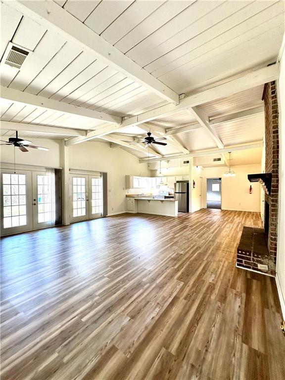 unfurnished living room featuring a ceiling fan, wood finished floors, visible vents, beam ceiling, and french doors