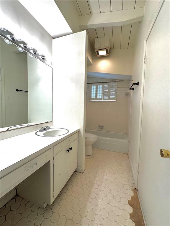 bathroom with beamed ceiling, toilet, vanity, and shower / tub combination