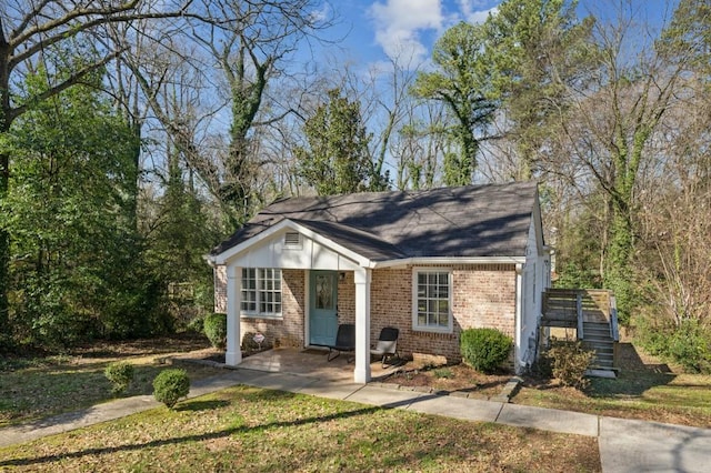 view of front facade with a front yard, brick siding, and stairs