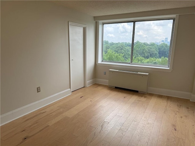 unfurnished room with radiator heating unit, light hardwood / wood-style flooring, and a textured ceiling