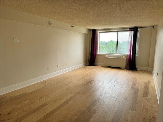 empty room featuring radiator heating unit, a textured ceiling, and light hardwood / wood-style flooring