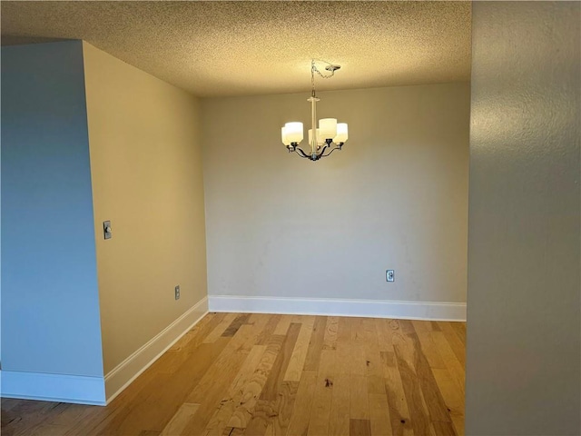 spare room with hardwood / wood-style floors, a notable chandelier, and a textured ceiling