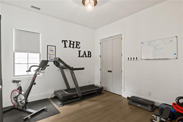 exercise area with visible vents, baseboards, and wood finished floors