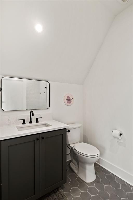 bathroom with tile patterned floors, toilet, baseboards, vanity, and vaulted ceiling