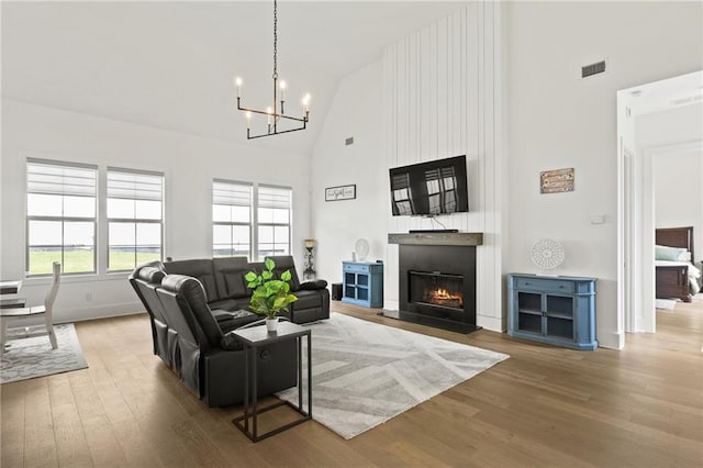 living area featuring wood finished floors, visible vents, high vaulted ceiling, a warm lit fireplace, and a notable chandelier