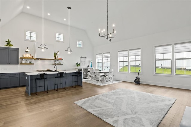 interior space with open shelves, a kitchen island with sink, gray cabinets, light countertops, and light wood-style floors