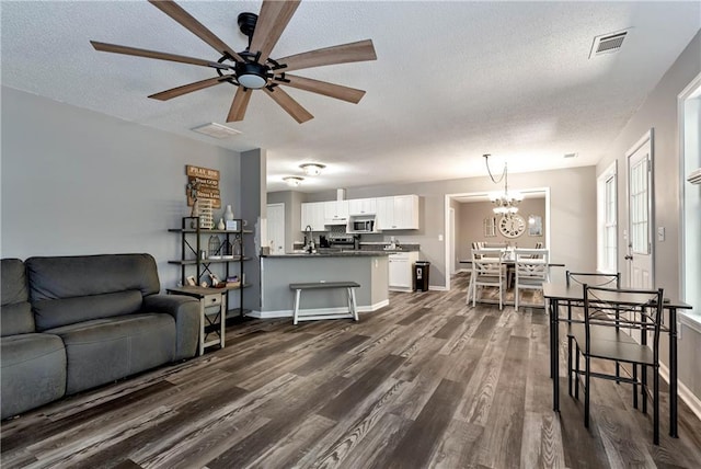 living room featuring ceiling fan with notable chandelier, dark wood-style floors, a textured ceiling, and visible vents