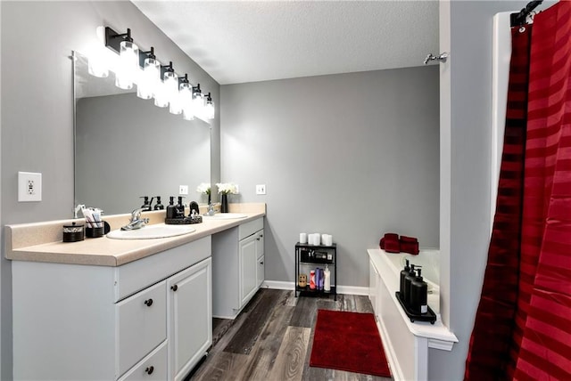 full bathroom with a textured ceiling, vanity, a garden tub, and wood finished floors