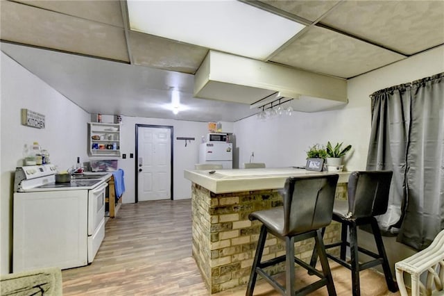 kitchen featuring a drop ceiling, light hardwood / wood-style flooring, a kitchen breakfast bar, white electric stove, and kitchen peninsula