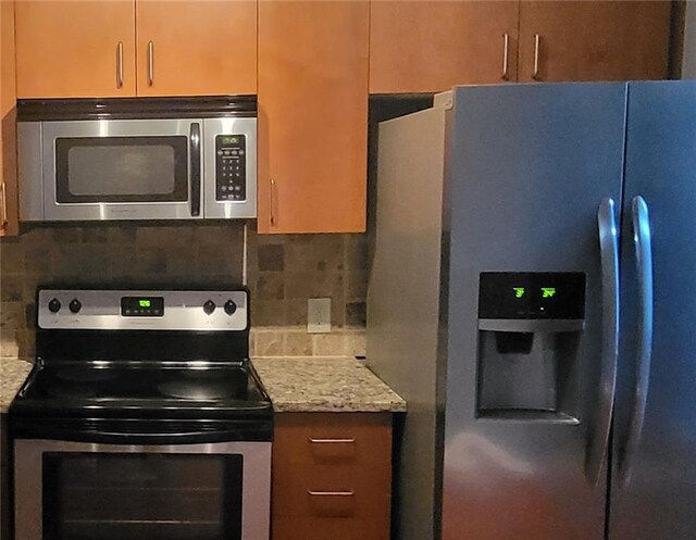 kitchen with light stone countertops, stainless steel appliances, and backsplash