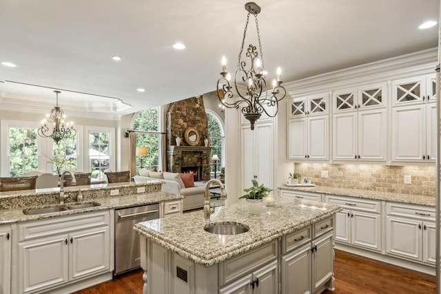 kitchen with white cabinetry, stainless steel dishwasher, a stone fireplace, and sink