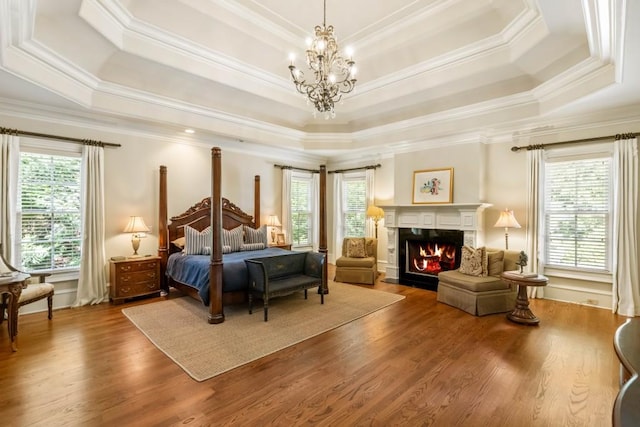 bedroom featuring a notable chandelier, a raised ceiling, a premium fireplace, and ornamental molding