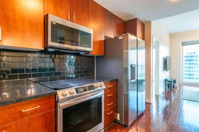 kitchen with wood-type flooring, appliances with stainless steel finishes, dark stone countertops, and backsplash