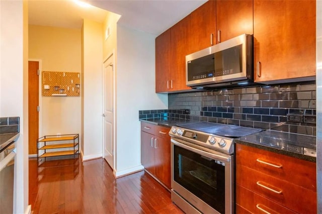 kitchen with stainless steel appliances, dark hardwood / wood-style floors, decorative backsplash, and dark stone counters