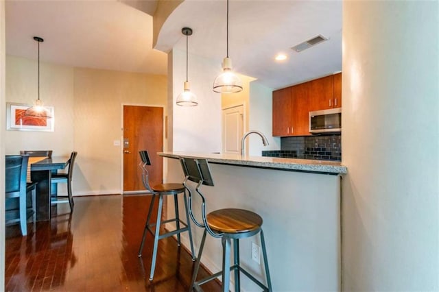 kitchen featuring a breakfast bar, dark hardwood / wood-style floors, decorative light fixtures, tasteful backsplash, and kitchen peninsula