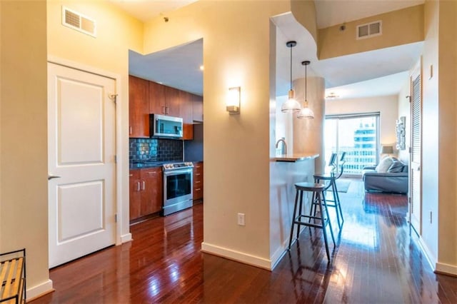 kitchen with dark wood-type flooring, a kitchen bar, decorative light fixtures, appliances with stainless steel finishes, and backsplash