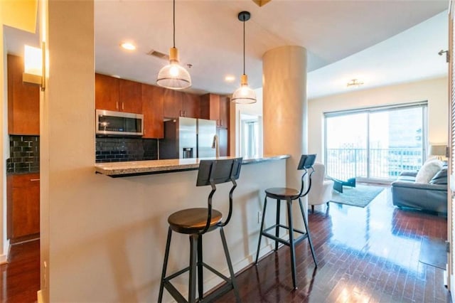 kitchen featuring dark wood-type flooring, a breakfast bar area, kitchen peninsula, stainless steel appliances, and decorative backsplash