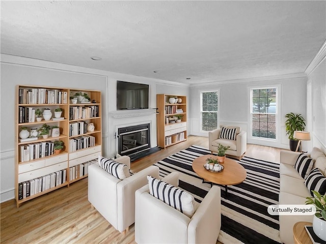 living area with light wood-style floors, built in shelves, ornamental molding, and a glass covered fireplace