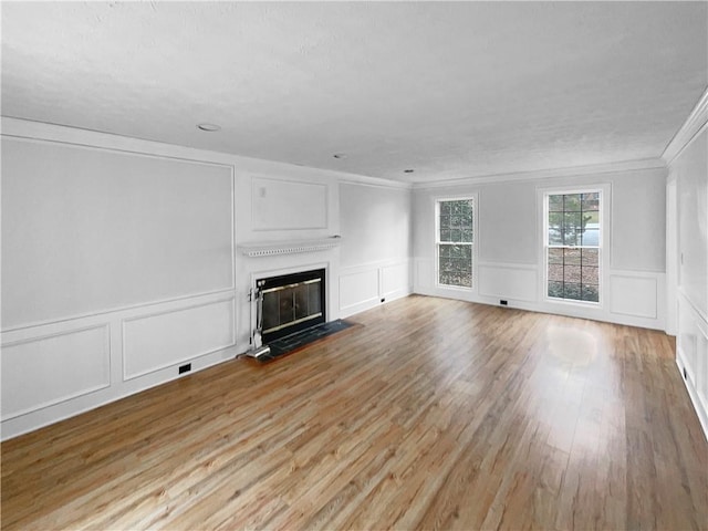 unfurnished living room with a fireplace with flush hearth, light wood-type flooring, crown molding, and a decorative wall