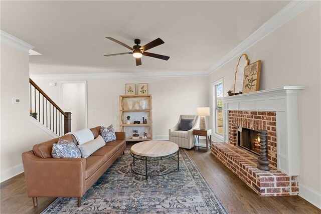 living room featuring ceiling fan, dark wood-type flooring, crown molding, and a brick fireplace