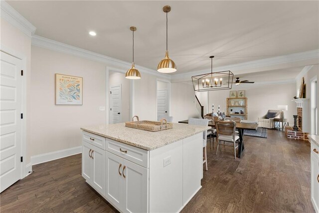 kitchen featuring white cabinetry, a brick fireplace, hanging light fixtures, a breakfast bar, and a center island