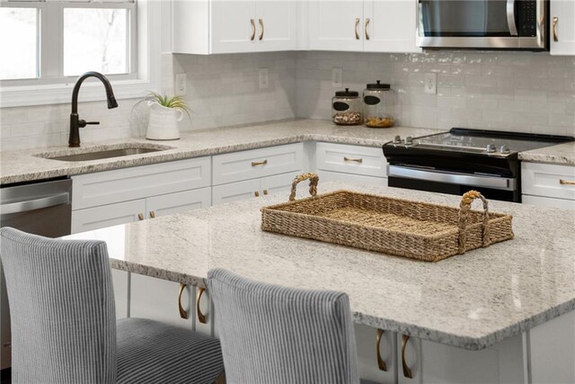 kitchen featuring light stone countertops, appliances with stainless steel finishes, white cabinetry, tasteful backsplash, and sink