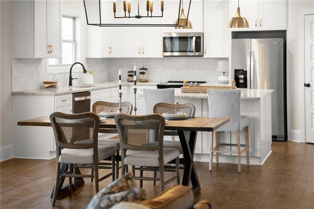 kitchen with a kitchen island, hanging light fixtures, light stone countertops, appliances with stainless steel finishes, and a kitchen breakfast bar