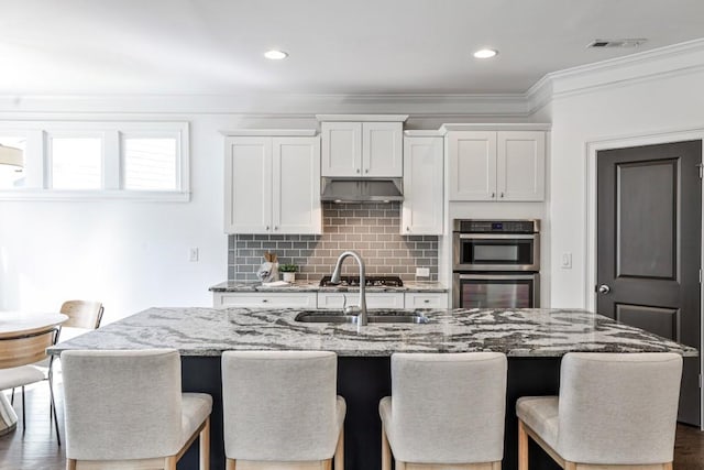 11760 Stratham Dr, Alpharetta, GA 30009 - kitchen featuring appliances with stainless steel finishes, under cabinet range hood, decorative backsplash, ornamental molding, and light stone counters