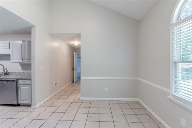 1406 Windy Ridge Ct SE, Conyers, GA 30013 - kitchen featuring stainless steel dishwasher, plenty of natural light, light tile patterned floors, baseboards, and lofted ceiling