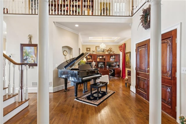 entrance foyer featuring decorative columns, a high ceiling, ornamental molding, wood finished floors, and stairs