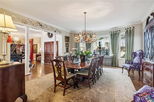 dining area with ornamental molding, a notable chandelier, ornate columns, and wood finished floors