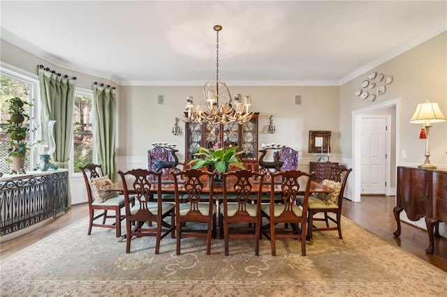 dining space with crown molding, wainscoting, a notable chandelier, and wood finished floors