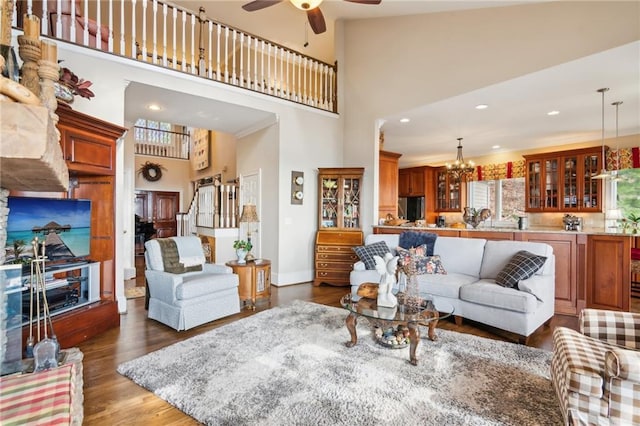 living room with dark wood finished floors, recessed lighting, a high ceiling, baseboards, and ceiling fan with notable chandelier