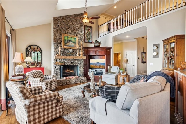 living room with high vaulted ceiling, light wood-type flooring, ceiling fan, and a stone fireplace