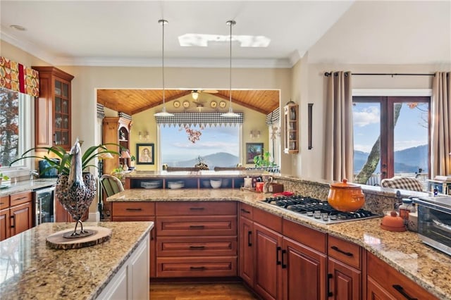 kitchen with glass insert cabinets, decorative light fixtures, light stone countertops, stainless steel gas stovetop, and a mountain view