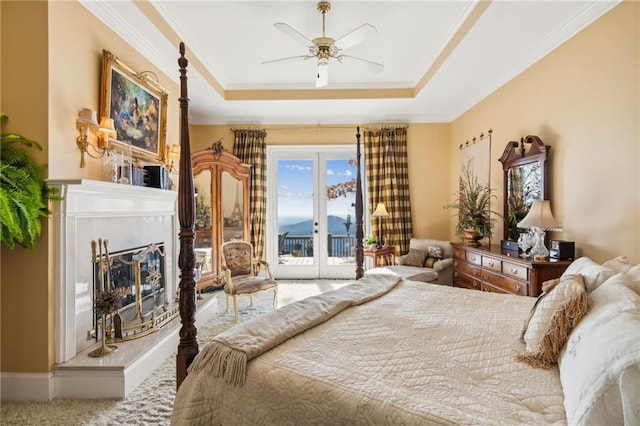 bedroom with a tray ceiling, access to outside, a glass covered fireplace, and french doors