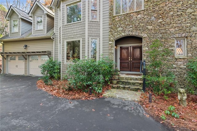 view of exterior entry with aphalt driveway, stone siding, and a garage