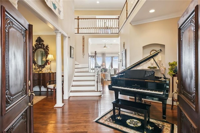 foyer featuring dark wood finished floors, stairway, ornamental molding, ceiling fan, and ornate columns