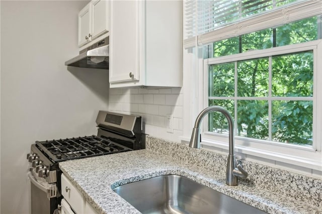 kitchen featuring white cabinetry, stainless steel gas stove, light stone countertops, decorative backsplash, and sink