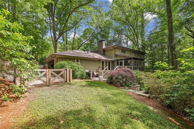 rear view of house with a chimney, a gate, a sunroom, fence, and a yard