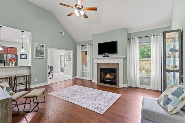 living area featuring ceiling fan, a fireplace, dark wood finished floors, high vaulted ceiling, and baseboards