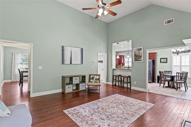 living room with a ceiling fan, high vaulted ceiling, wood finished floors, a chandelier, and plenty of natural light